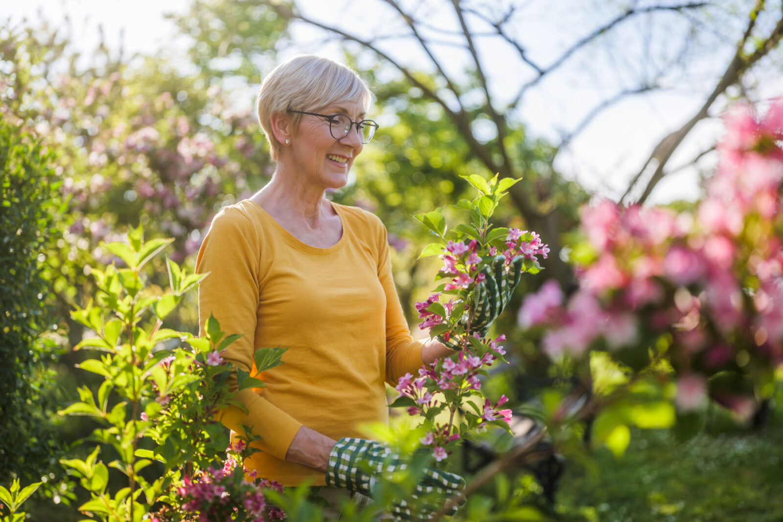 Happy senior woman smiling and enjoying the spring weather while tending to her outdoor flower garden.