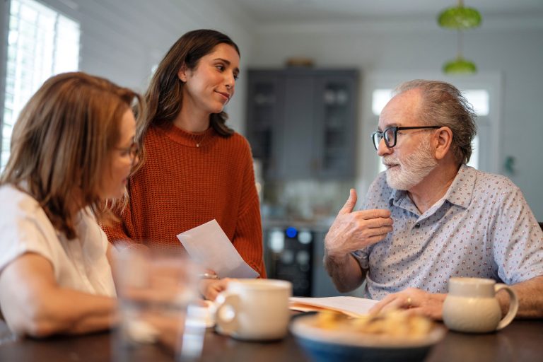 Adult daughters lovingly conversing with their father over breakfast inside the home.
