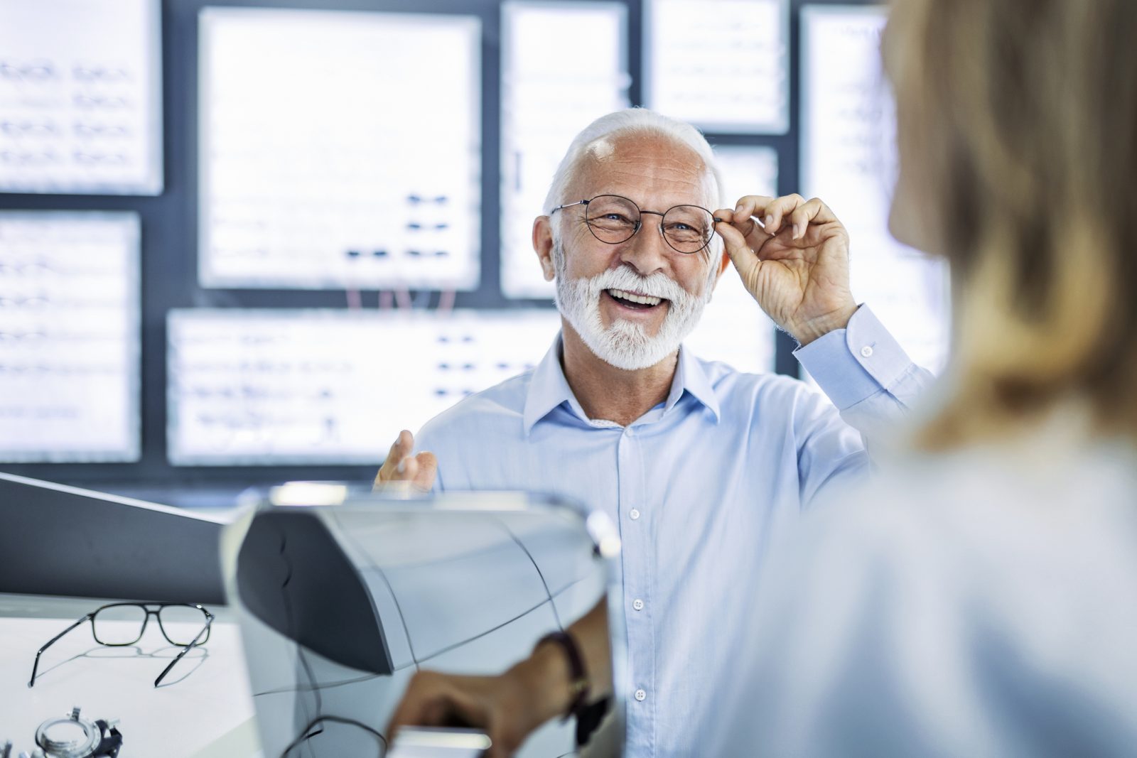 Senior man smiling while testing out glasses during his vision exam with an ophthalmologist