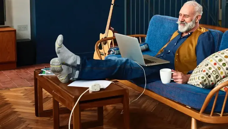 Senior man sitting on the couch researching the cost of home care in Tallahassee Florida on his laptop.