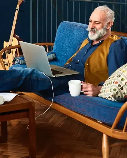 Senior man sitting on the couch researching the cost of home care in Tallahassee Florida on his laptop.