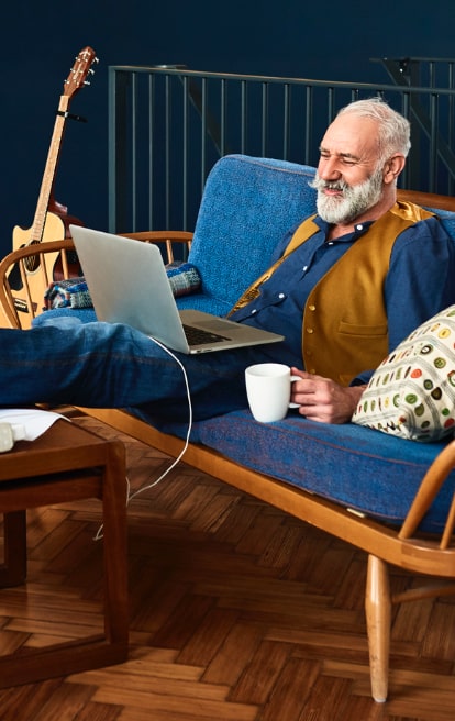 Senior man sitting on the couch researching the cost of home care in Tallahassee Florida on his laptop.
