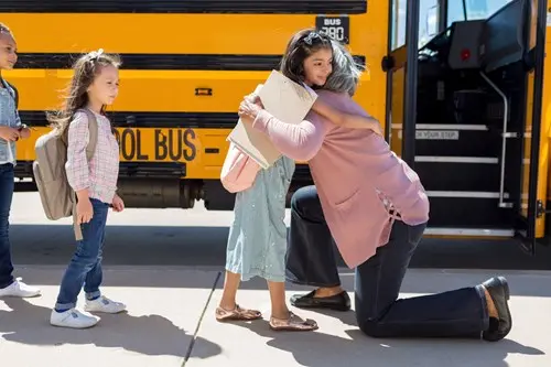 grandma hugging goodbye to young granddaughter getting on the bus for school