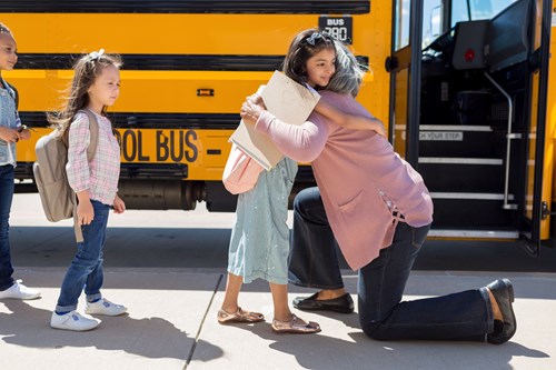 grandma hugging goodbye to young granddaughter getting on the bus for school