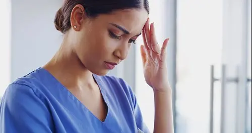 caregiver female with head tilted down and fingertips supporting head eyes closed sad