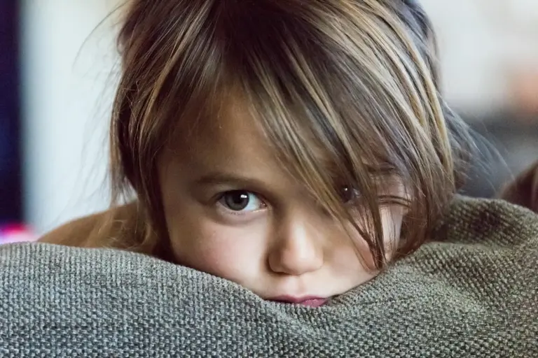 young girl with chin on pillow staring with big brown eyes