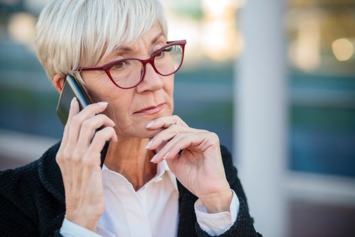 sophistivated senior woman with short grey hair, glasses, talking on cell phone
