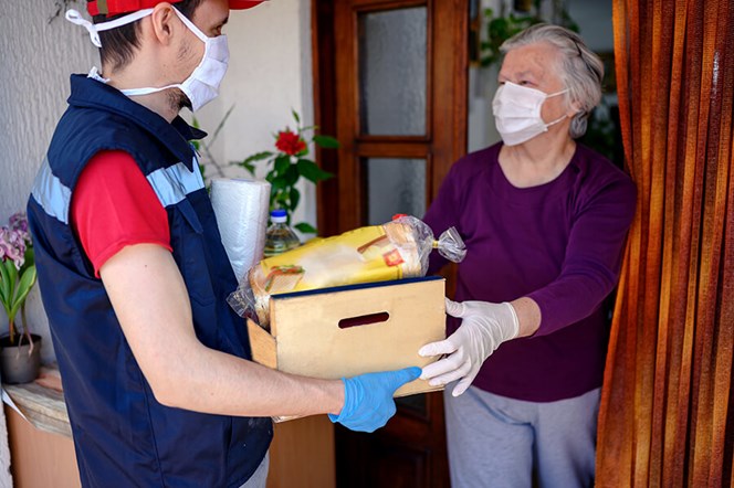 young man delivering groceries to masked senior woman at her front door