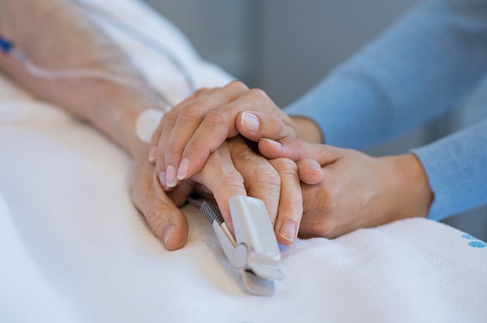elderly woman hand with oxygen monitor on finger being held by another hand