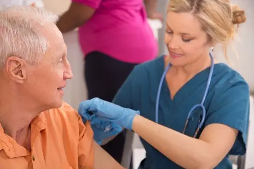nurse giving senior man a flu shot in his left arm