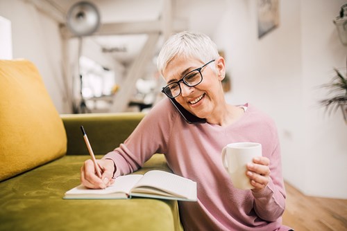happy lady writing in journal, on phone and holding cup