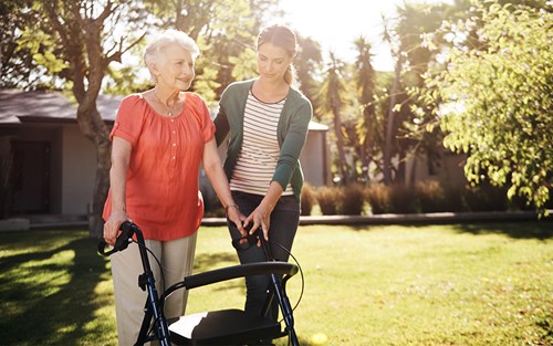 happy senior woman with walker and caregiver outside