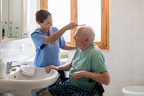 female caregiver grooming senior man in bathroom