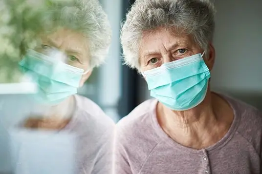 lonely caucasion senior woman mask on staring out the window aimlessly