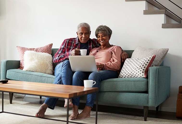 senior couple sitting on couch looking at laptop drinking coffee