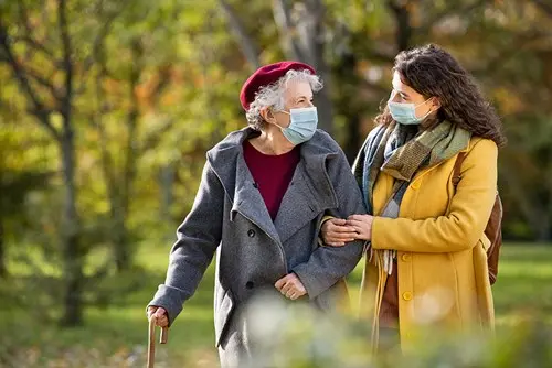 senior woman and caregiver walking outside wearing masks