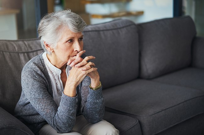 senior woman alone on couch looking pensive