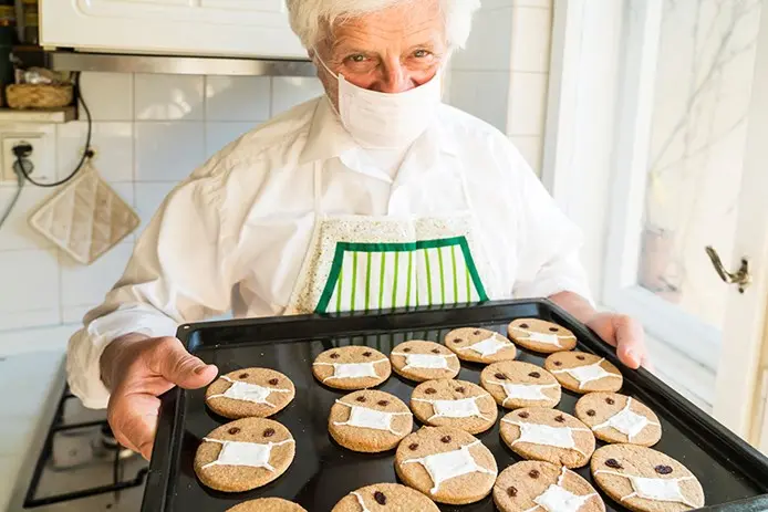 senior woman in mask with tray of cookies decorated with masks