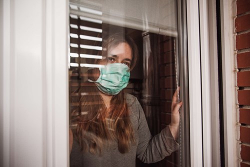 woman with face mask on looking out window