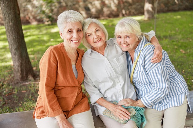 Three senior women smiling sitting outdoors happy