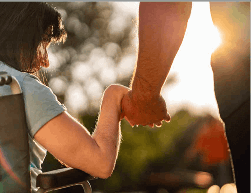 30ish woman in wheelchair with man walking beside her holding her hand