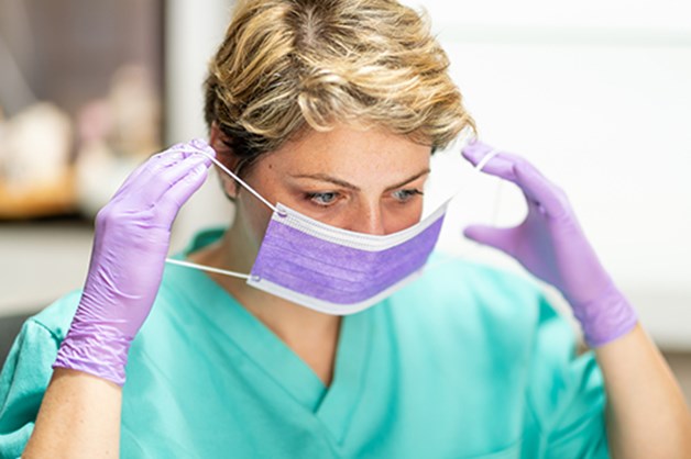 Caregiver female short brown hair wearing scrubs and protective gloves putting a face mask on