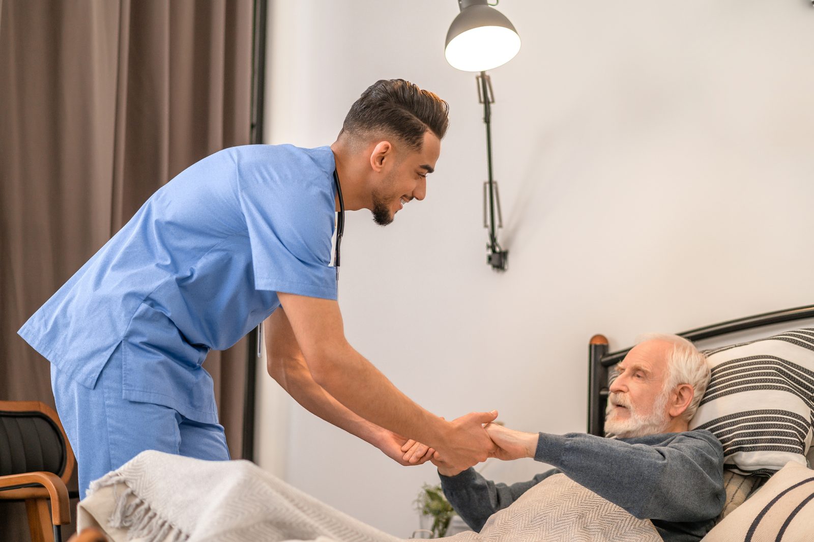 SYNERGY HomeCare helping an elderly man out of bed.
