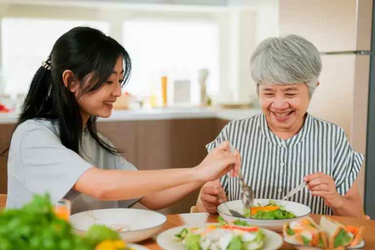 A woman serves healthy food to her senior mother before eating together in their kitchen.