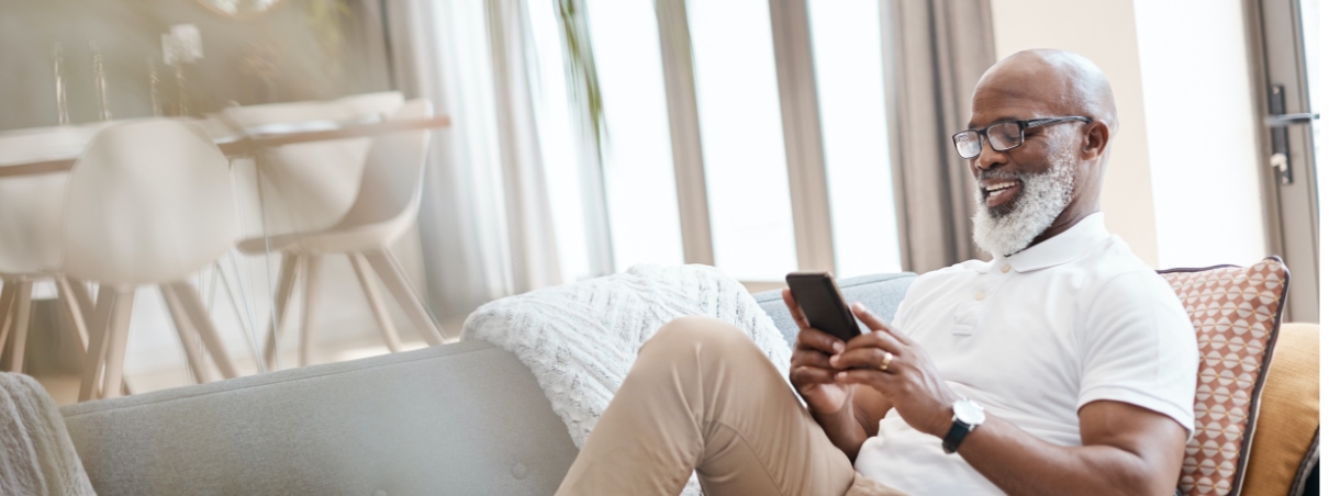 Senior gentleman sitting on the couch and smiling while looking at his phone.