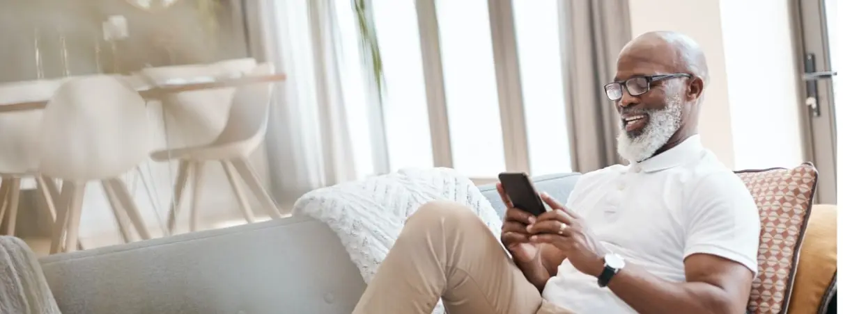 Senior gentleman sitting on the couch and smiling while looking at his phone.