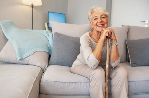Senior woman sitting on the couch holding he cane