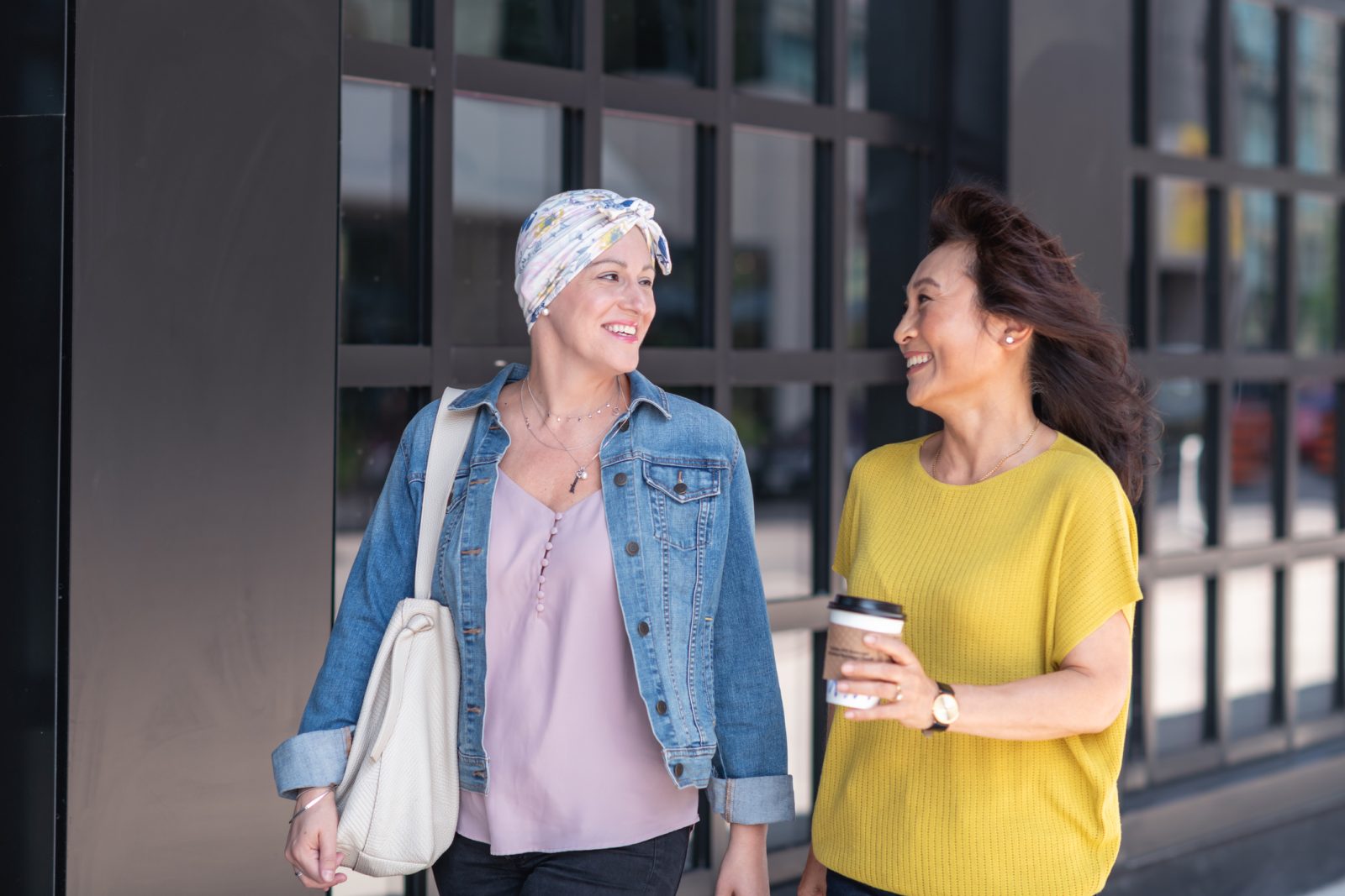 Woman with cancer smiling with a friend as they both walk and talk with each other outside