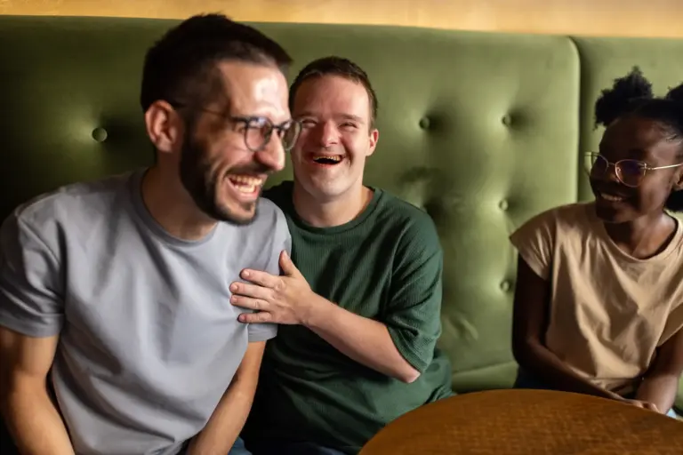 Three young adults, including a man with down syndrome, sitting and laughing together in a cafe
