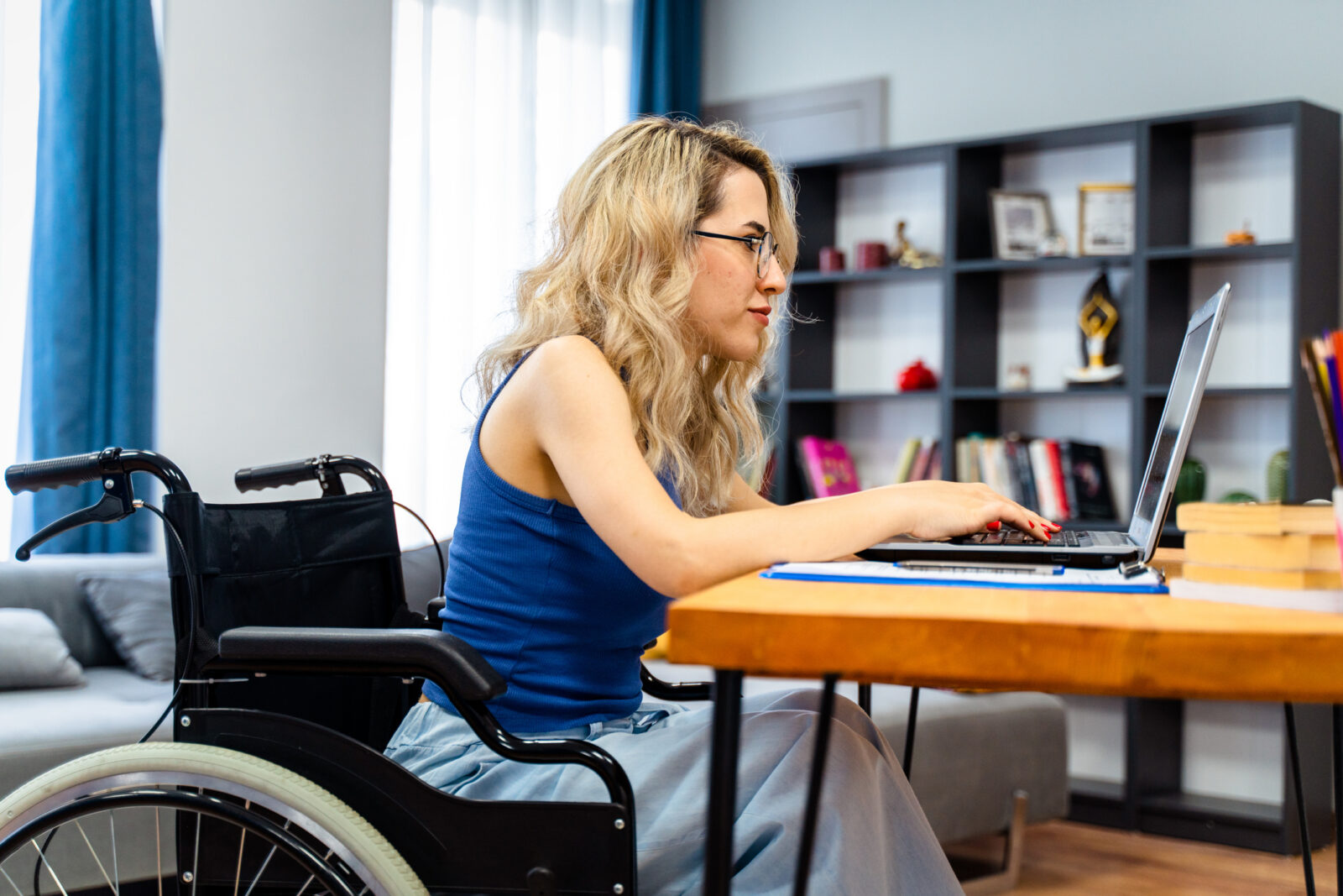 A blonde woman in a wheelchair uses her laptop, researching options to deal with chronic illness and disability.