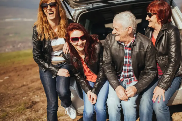 Happy family on summer road trip with aging loved ones, smiling together in back of SUV at scenic stop