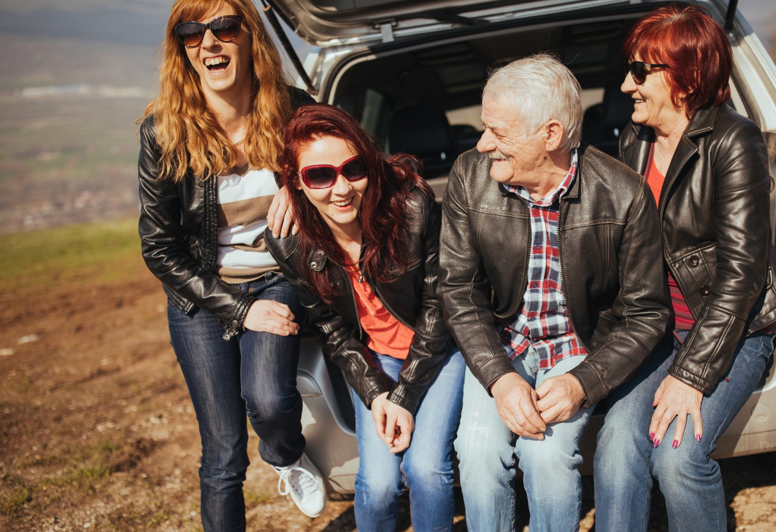 Happy family on summer road trip with aging loved ones, smiling together in back of SUV at scenic stop