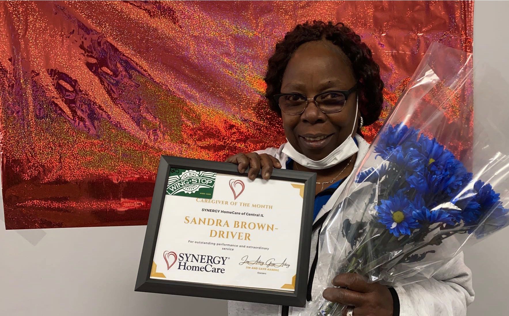 Caregiver of the month Sandra brown hold her award and flowers with a big beautiful smile