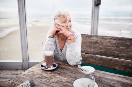 A senior woman with a cup of coffee at the beach looking off into the distance
