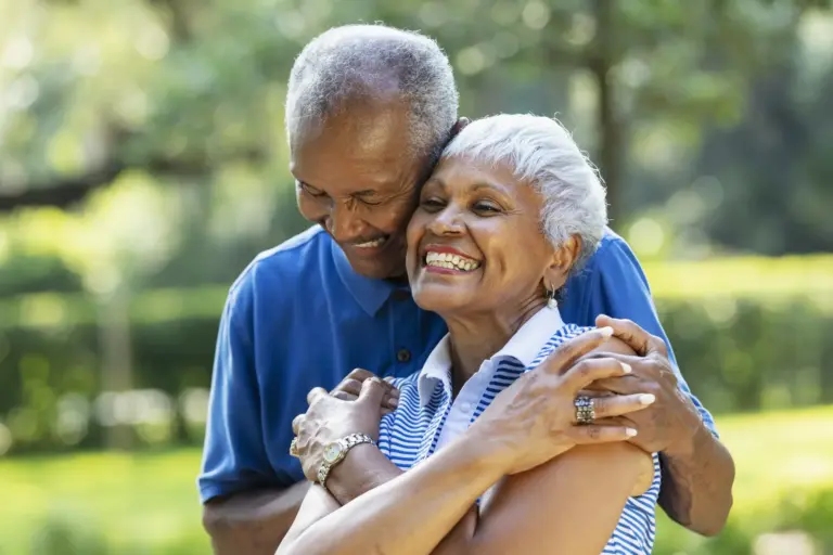 Two African American seniors embracing and smiling outdoors