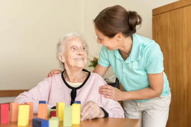 Senior woman with dementia smiles at her loved one, who is helping with a fun activity to support brain health.