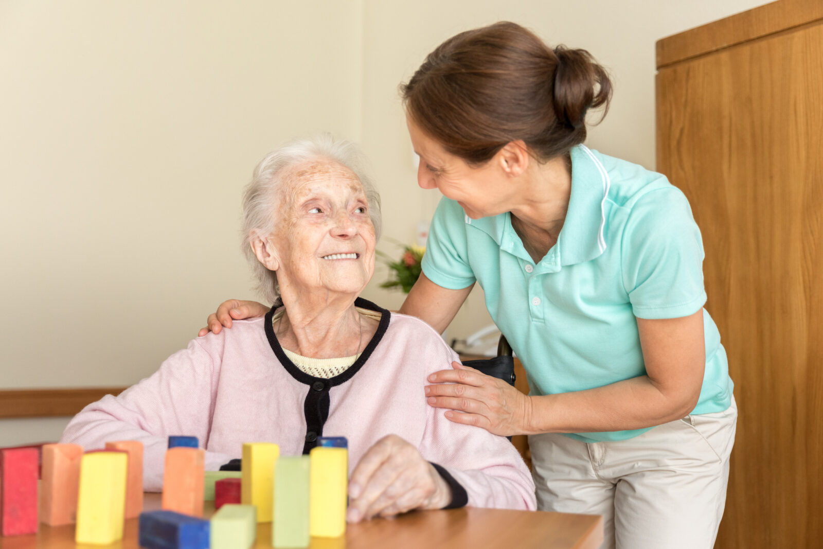 Senior woman with dementia smiles at her loved one, who is helping with a fun activity to support brain health.