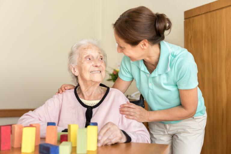 Senior woman with dementia smiles at her loved one, who is helping with a fun activity to support brain health.