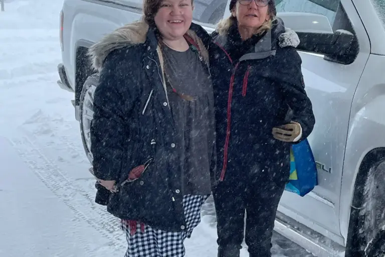 Caregiver and SYNERG HomeCare of Central IL owner Gaye aaberg pose by a pickup truck bundled in snow gear in a snowstorm