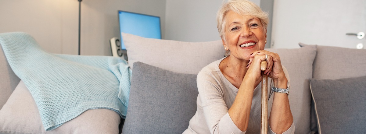 Senior woman sitting on the couch holding her walking cane.