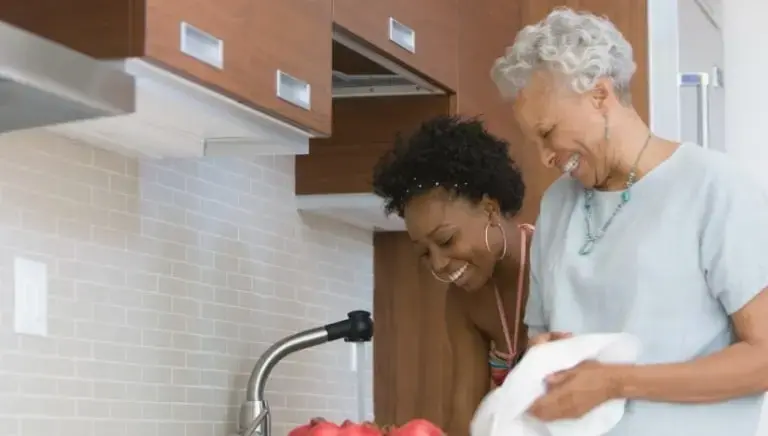 A senior woman in Charleston, SC washing dishes in the kitchen with the help of her SYNERGY HomeCare caregiver.