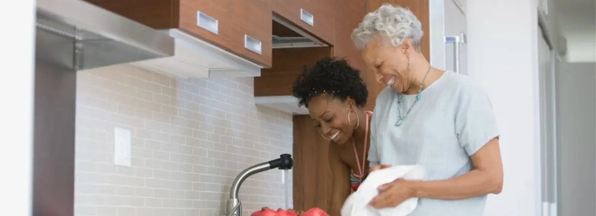 A senior woman in Charleston, SC washing dishes in the kitchen with the help of her SYNERGY HomeCare caregiver.