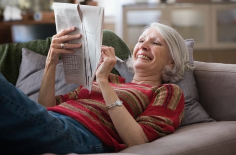 senior woman enjoying doing a crossword puzzle while laying on the couch