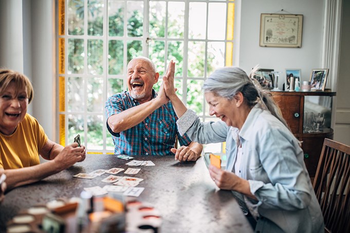 3 seniors laughing playing cards at a table