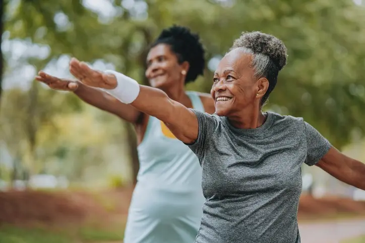 Two senior women doing yoga together in a park.
