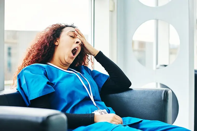 caregiver sitting in comfy chair yawning with left hand on forehead